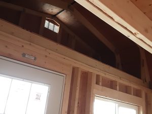 A Lofted Dutch Cabin - 1456 showcases a partially constructed wooden room with exposed framing and a multi-pane window. The unfinished ceiling reveals the beams and structure of the roof, allowing natural light to beautifully illuminate the space.