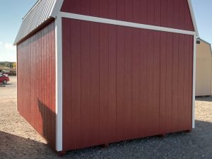 The Lofted Dutch Barn - 2113 in classic red and white stands proudly on a gravel surface under the clear blue sky.