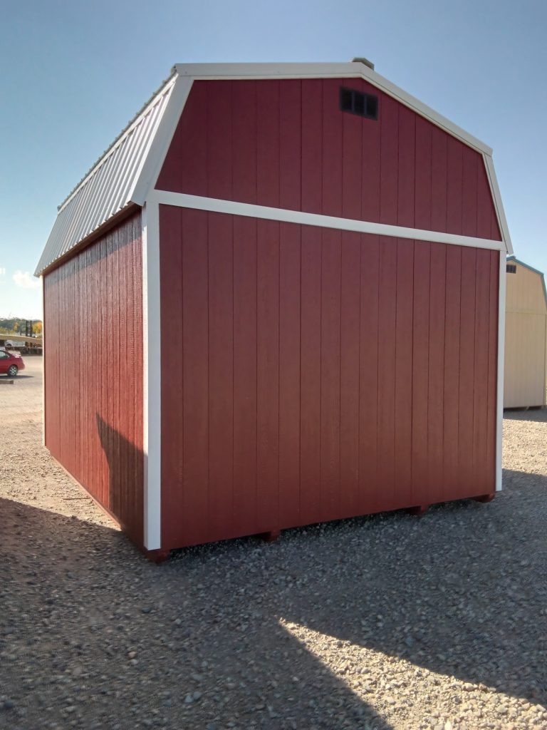 The Lofted Dutch Barn - 2113 in classic red and white stands proudly on a gravel surface under the clear blue sky.