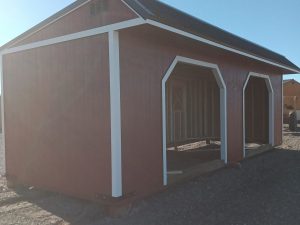 The Horseman - 2303, a red wooden shed with white trim and an open interior that evokes the charm of a rustic horseman's retreat, is nestled on a gravel lot beneath the vast blue sky.