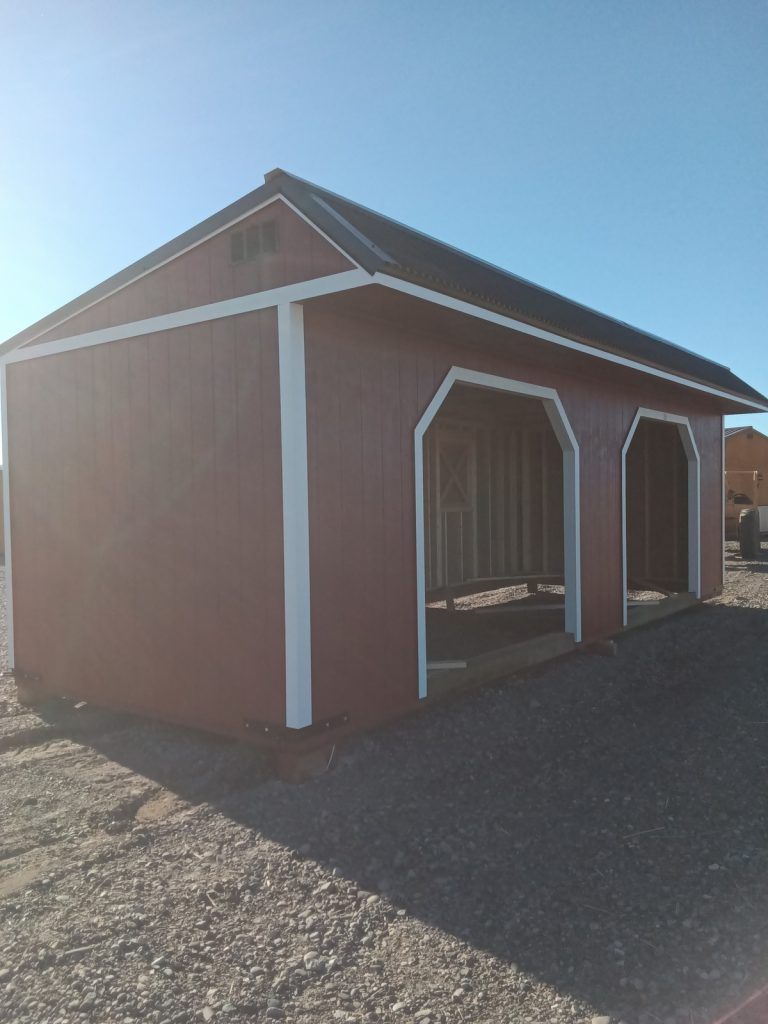The Horseman - 2303, a red wooden shed with white trim and an open interior that evokes the charm of a rustic horseman's retreat, is nestled on a gravel lot beneath the vast blue sky.